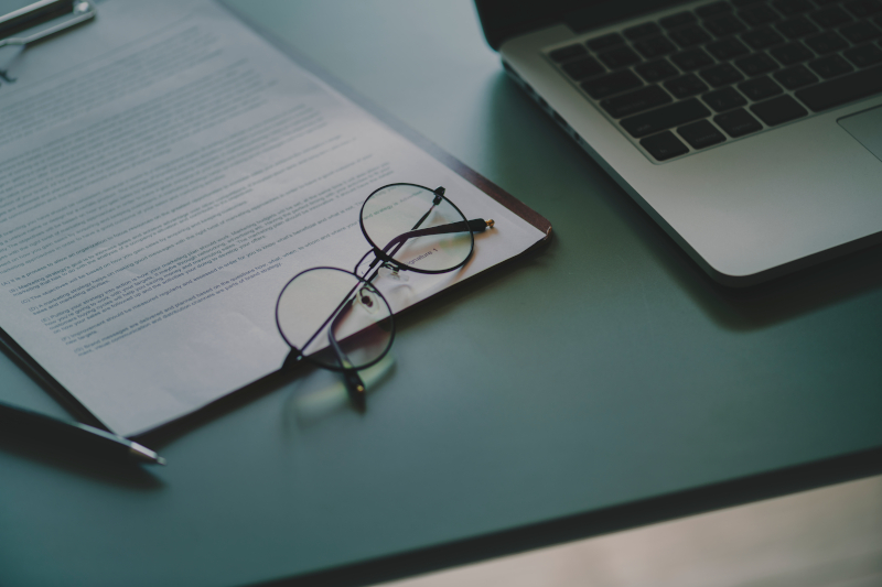 Picture of document on clipboard with glasses and laptop